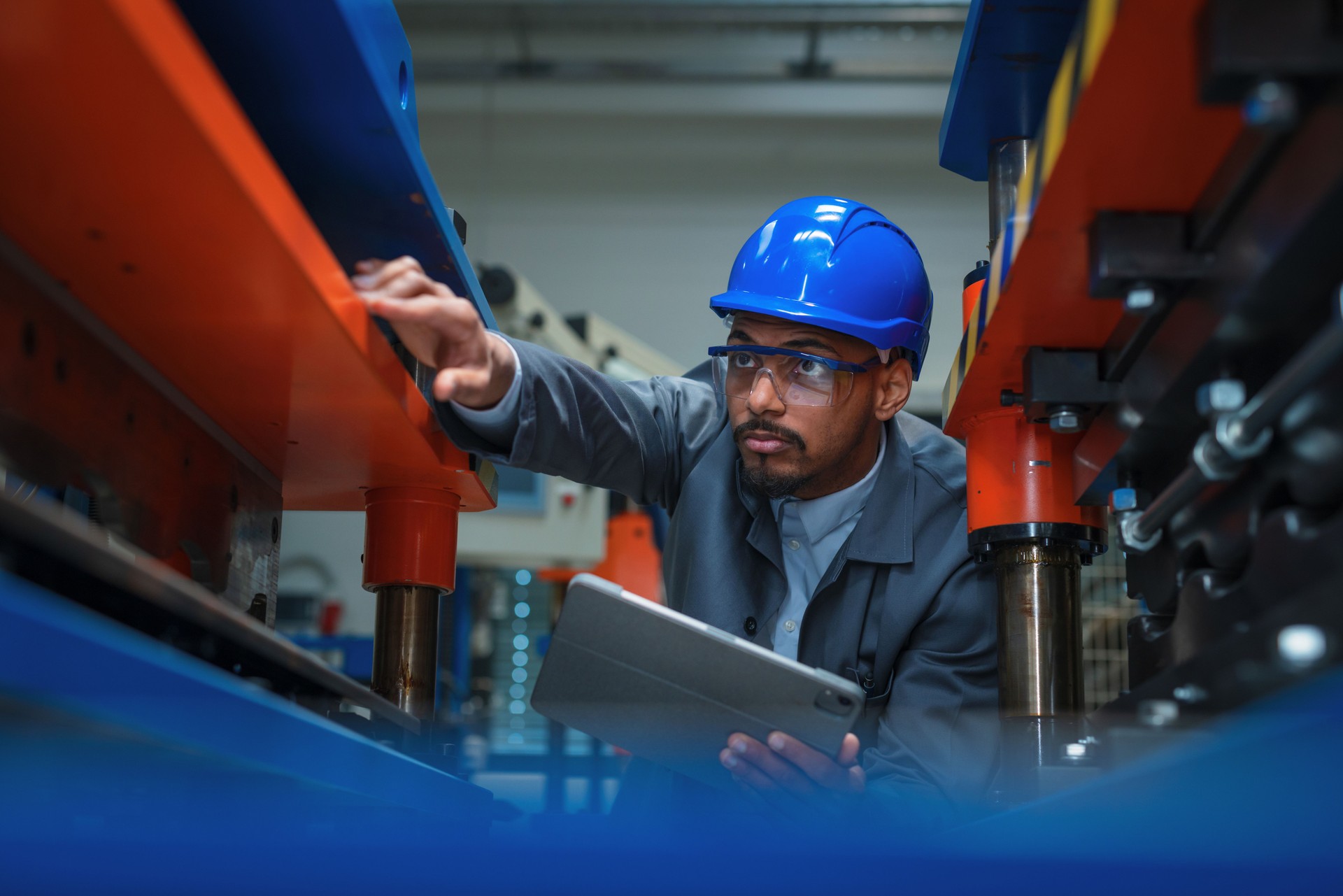 Engineer with a blue helmet and safety glasses, checking manufacturing machinery